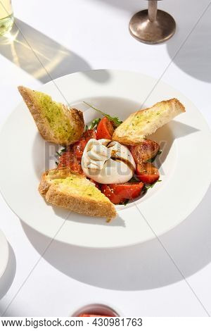 Traditional Italian salad with Burrata cheese and tomatoes. Fancy caprese with burrata cheese, cherry tomatoes, pesto and balsamic sauces. Summer dish with mozzarella cheese on white table with shadow