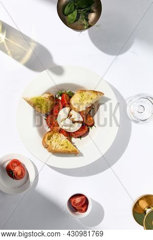 Traditional Italian salad with Burrata cheese and tomatoes. Fancy caprese with burrata cheese, cherry tomatoes, pesto and balsamic sauces. Summer dish with mozzarella cheese on white table with shadow