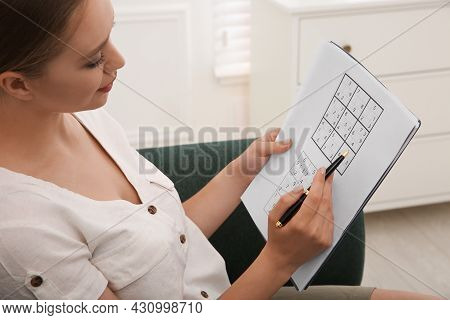 Young Woman Solving Sudoku Puzzle On Sofa Indoors, Closeup