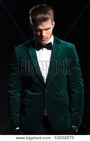 young man in a green velvet suit is looking down on black background