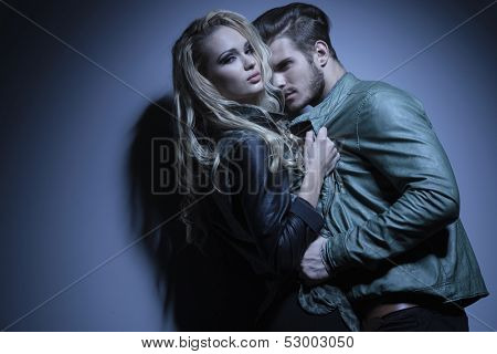 woman in leather jacket is pulling her lover closer and looks at the camera