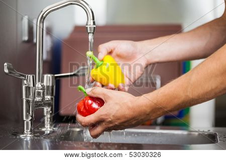 Kitchen porter washing pepper under running tap in professional kitchen