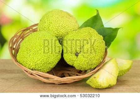 Osage Orange fruits (Maclura pomifera) in basket, on wooden table, on nature background