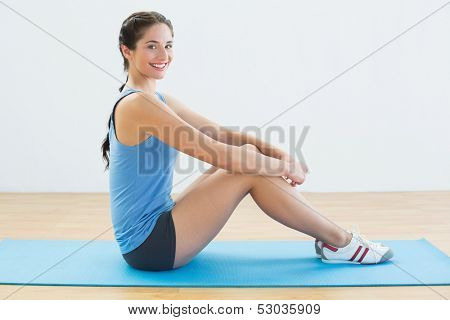Full length portrait of a fit young woman sitting upright on exercise mat