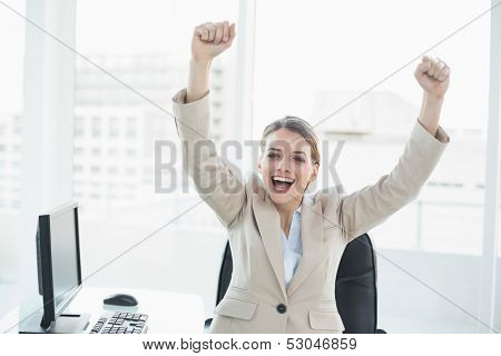 Happy cheering woman raising her arms sitting on her swivel chair looking at camera
