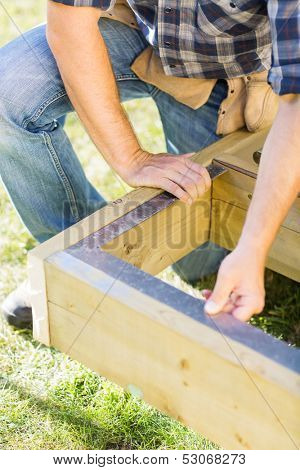 Mid section of manual worker measuring wood with scale at construction site