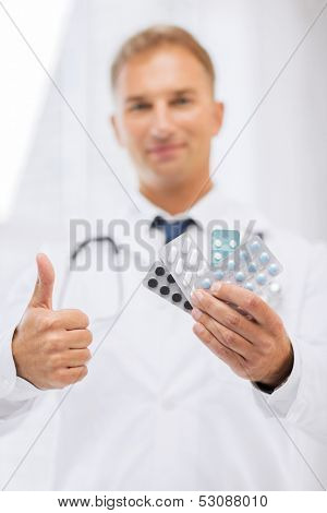healthcare, medical and pharmacy concept - male doctor with packs of pills showing thumbs up