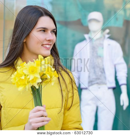 Portrait of young beautiful woman with sping flowers, outdoor over shopwindow with dummy.