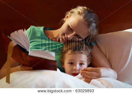 Young mother reading to her child in bed