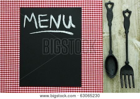 Chalkboard menu sign with cast iron spoon and fork on red checkered tablecloth