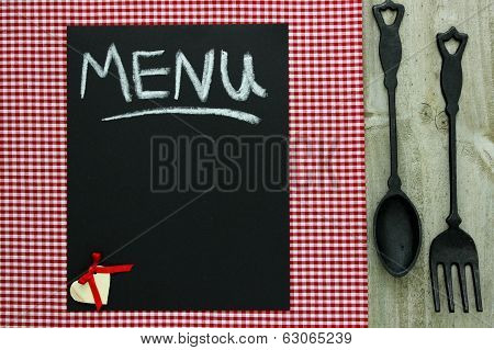 Chalkboard menu sign with cast iron spoon and fork on red checkered tablecloth