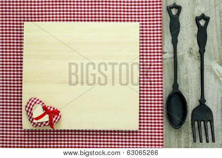 Blank wood menu sign with cast iron spoon and fork on red checkered tablecloth