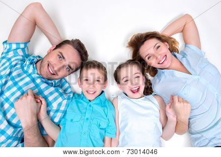 High angle portrait of caucasian happy smiling young family with two children lying down on white floor and looking at camera