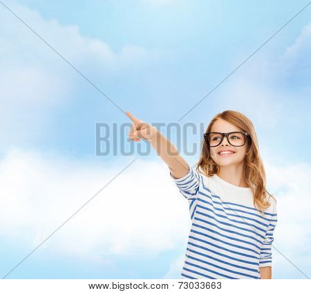 education, school and imaginary screen concept - cute little girl in eyeglasses pointing in the air or imaginary screen