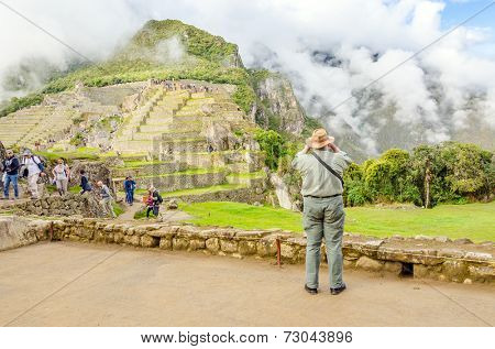 MACHU PICCHU, PERU - MAY 3, 2014 - crowds of tourist explore ruins of old city early in the morning while senior tourist takes photos