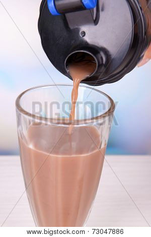 Shaker with protein shake and glass on table on bright background