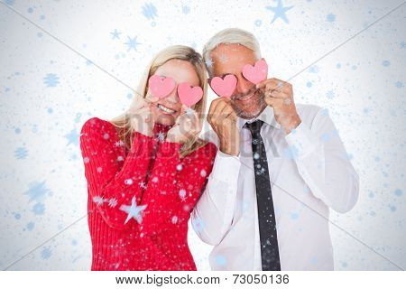 Silly couple holding hearts over their eyes against snow falling
