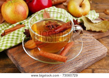 Composition of  apple cider with cinnamon sticks, fresh apples and autumn leaves on wooden background