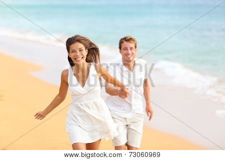 Couple on beach running having fun laughing in elegant casual beach wear. Happy multicultural multi-ethnic young lovers and friends by ocean on summer vacation holidays travel. Woman and man.