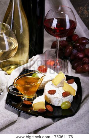 Supper consisting of Camembert and Brie cheese, honey, wine and grapes on napkin and wine barrel on curtain background