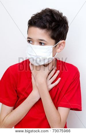  A sick young boy clutches his throat with face mask on.