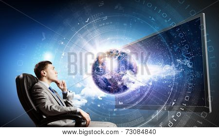 Young businessman sitting in chair behind tv. Elements of this image are furnished by NASA