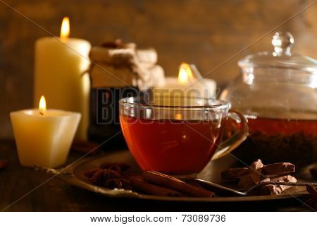Composition with tea in cup and teapot and candles on table, on wooden background