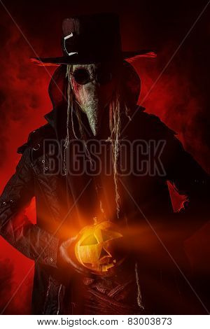Frightening plague doctor stands with a pumpkin. Medieval Europe. Halloween.