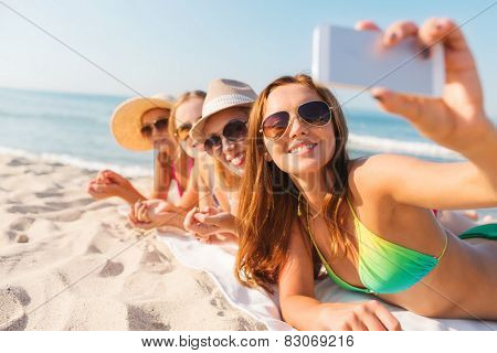 summer vacation, travel, technology and people concept - group of smiling women in sunglasses and hats making selfie with smartphone on beach
