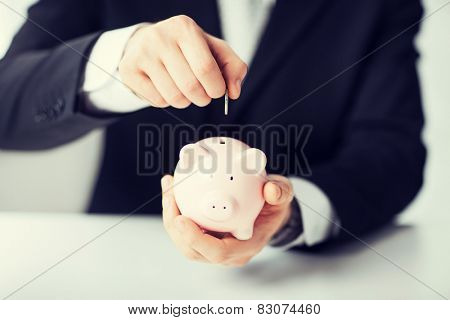picture of man putting coin into small piggy bank