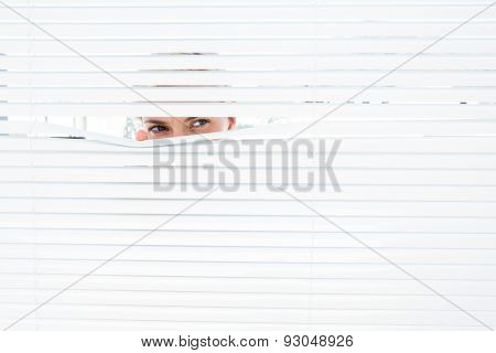 Curious blonde woman looking through venetian blind on a sunny day