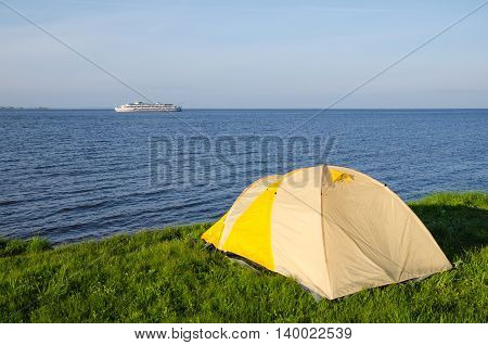 The River Kama. Tourist tent on the shore of the Kuibyshev reservoir. On the horizon floats a tourist motor ship.