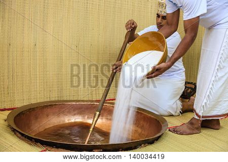 NIZWA, OMAN, MAY 27, 2016: factory worker pours sugar into a copper kettle for making of traditional Omani halwa