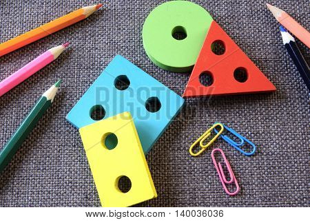 Back to school. Colored pencils, colored paper clips and colored geometric shapes lie on the textured fabric