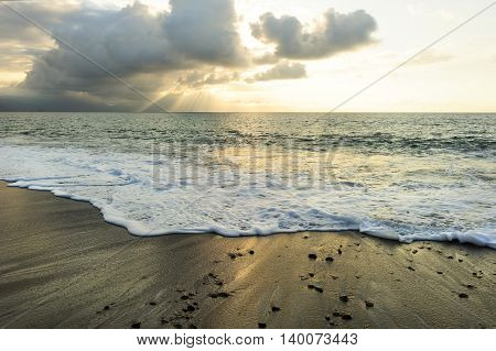 Ocean sunset sun rays is a bright uplifting seascape with sun beams breaking through the clouds as a gentle wave rolls to shore.