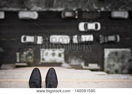 Close-up of man's feet standing on the edge of the roof. Top view on man's boots on the balcony of high building. Depression and instability concept. Crisis.