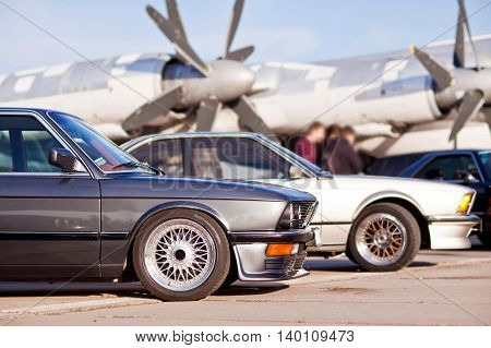 Right front side of two old european sport cars with plane on background.