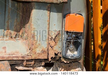 Old and rusty iron car. Broken tail lamp of the auto and the fence.