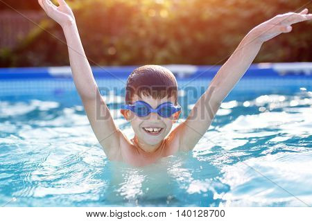 Happy little boy in goggles enjoying play in pool hurray summer holiday