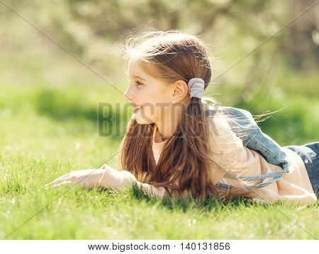 cute smiling little girl lying on the grass in park looking away
