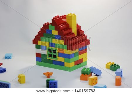 Colorful toy house with window roof and chimney. Around are colorful bricks in mess.
