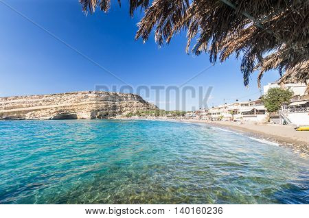 Matala beach on Crete island, Greece. Tourists relax and bath in crystal clear water of Matala in south of Creta. There are many caves near the beach.