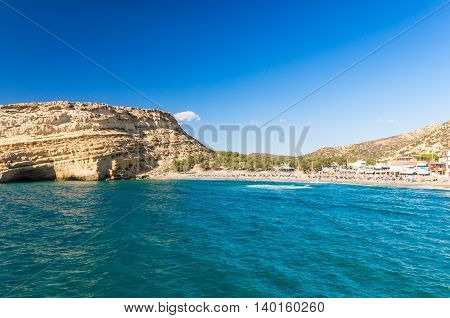 Matala beach on Crete island, Greece. Tourists relax and bath in crystal clear water of Matala in south of Creta. There are many caves near the beach.