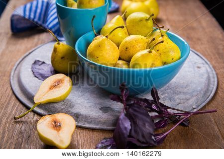 some raw ripe small yellow pears in blue dish on wooden background
