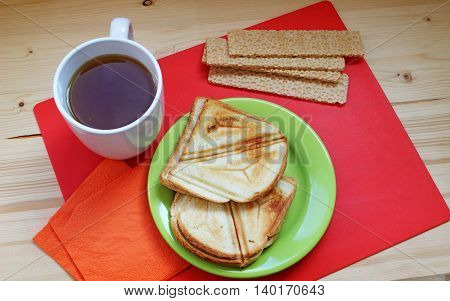 Breakfast on a red and wooden background. Crispbread sandwiches and cup of hot tea on the table - tasty meal.