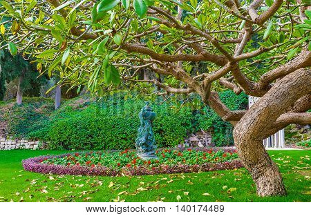 The view on the scenic flower bed with park sculpture with the spreading tree on the foreground Bahai Gardens Haifa Israel.