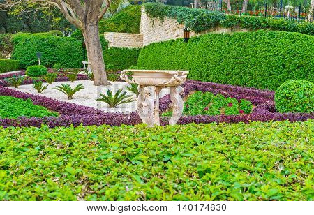 The white stone fountain decorated with the complex carvings among the greenery of Bahai Garden Haifa Israel.