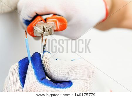 Electrican shortens electric wire using wire cutters.