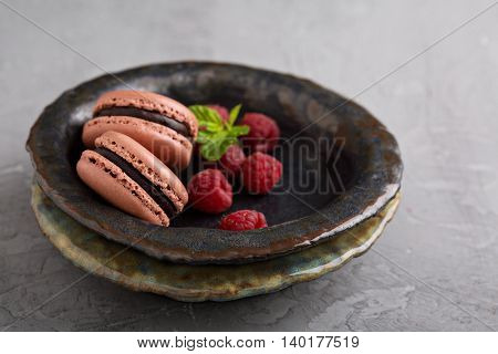 Chocolate french macarons with ganache filling on handmade ceramic plate