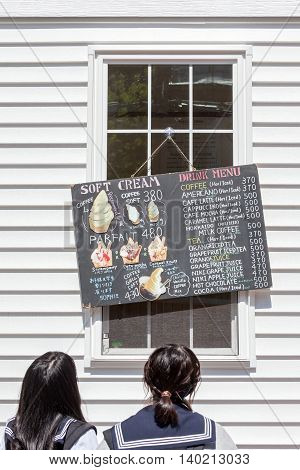 Otaru Hokkaido Japan: June 5 2016. Two Japanese teenagers reading Ice-cream and beverage menu board beside Otaru street.